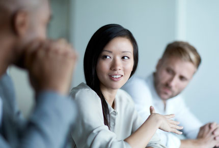 Two men listening to a woman speaking during a meeting.